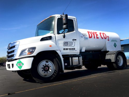 Front-left view of a white tanker truck with red 'DYE CO 2' lettering parked on asphalt under a blue sky