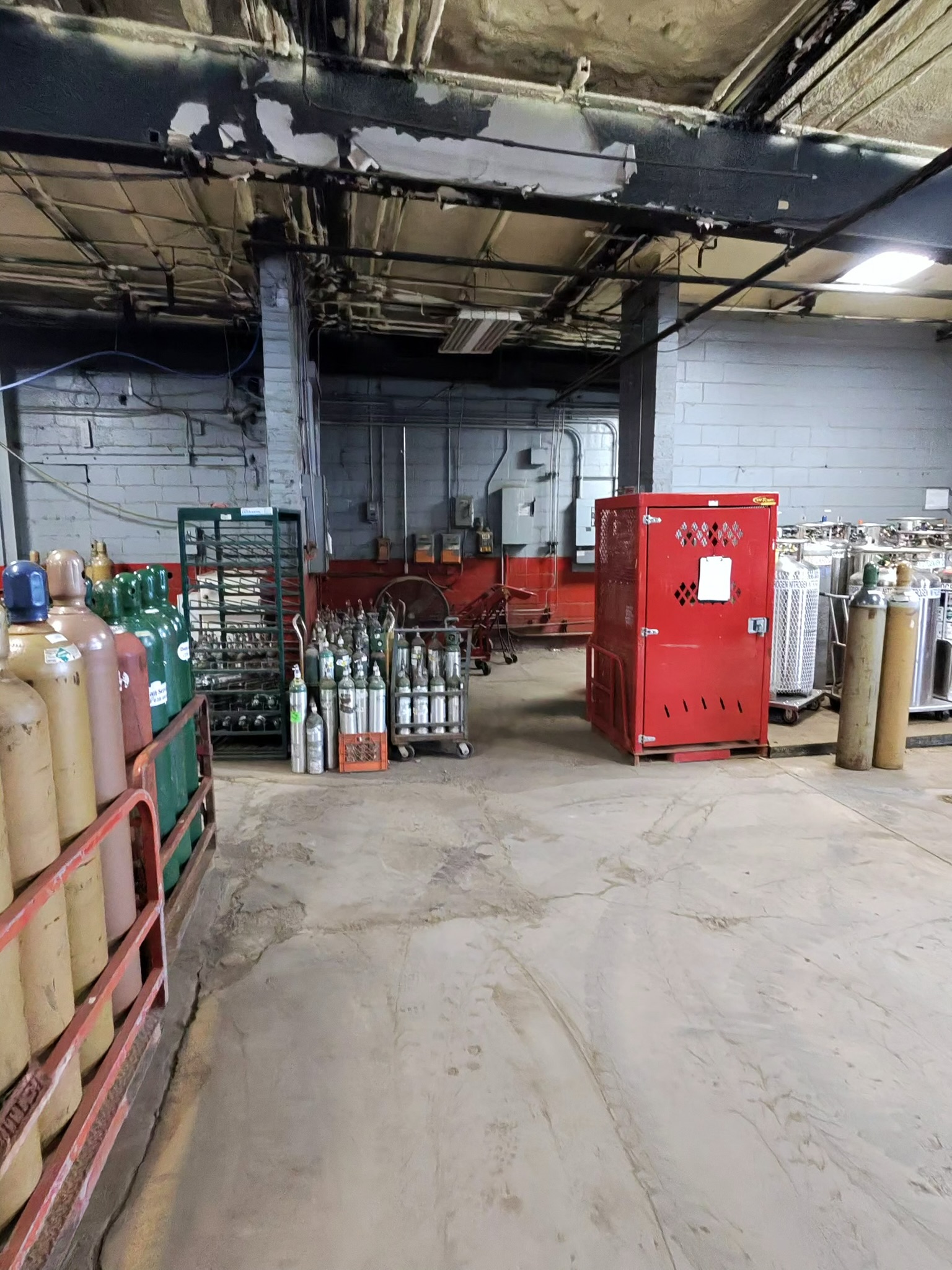 Industrial workshop scene with gas cylinders along the left wall and a red safety cabinet in the center-right area of the image.
