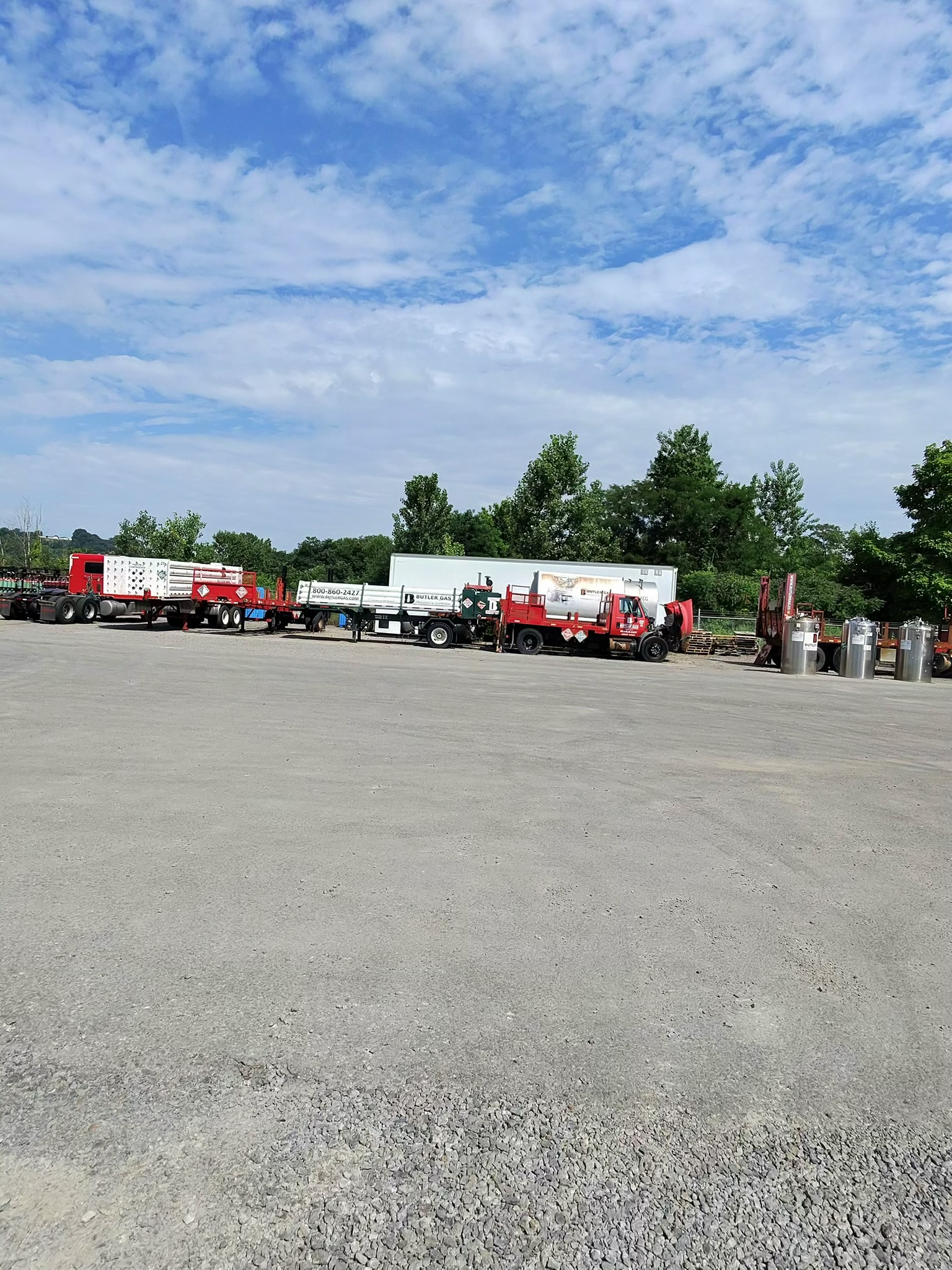 Row of red and white semi trucks and trailers in a truck yard beneath a partly cloudy blue sky.