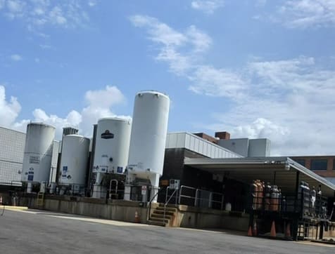 Industrial facility with multiple tall white storage tanks beside a brick building and loading dock under a blue sky.