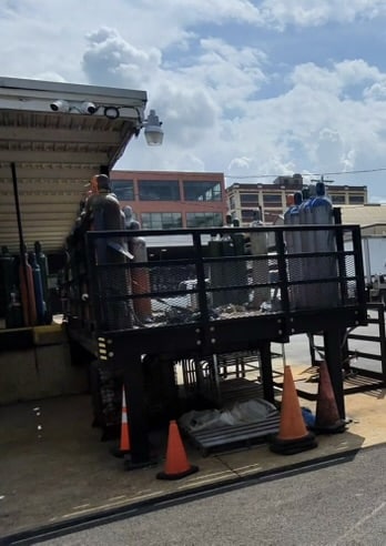 Two workers on a raised platform at a rooftop loading dock, with orange cones and equipment nearby.