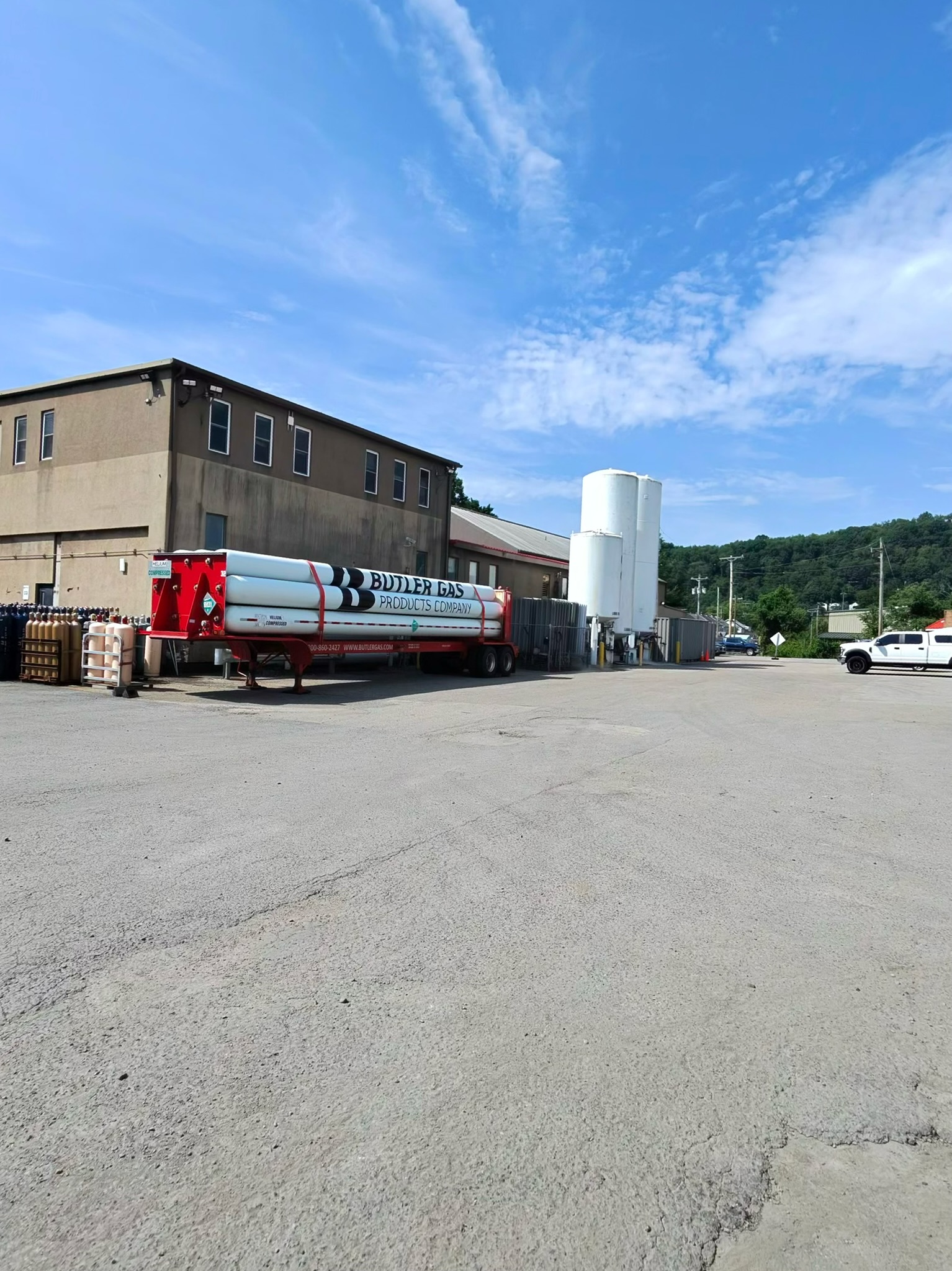 Industrial building and gas facility with a red Butler Gas trailer and stacked propane cylinders in the foreground under a blue sky.
